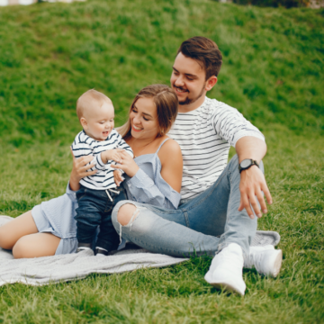 młodzi rodzice z dzieckiem na kocu podczas rodzinnego pikniku na zielonej trawie